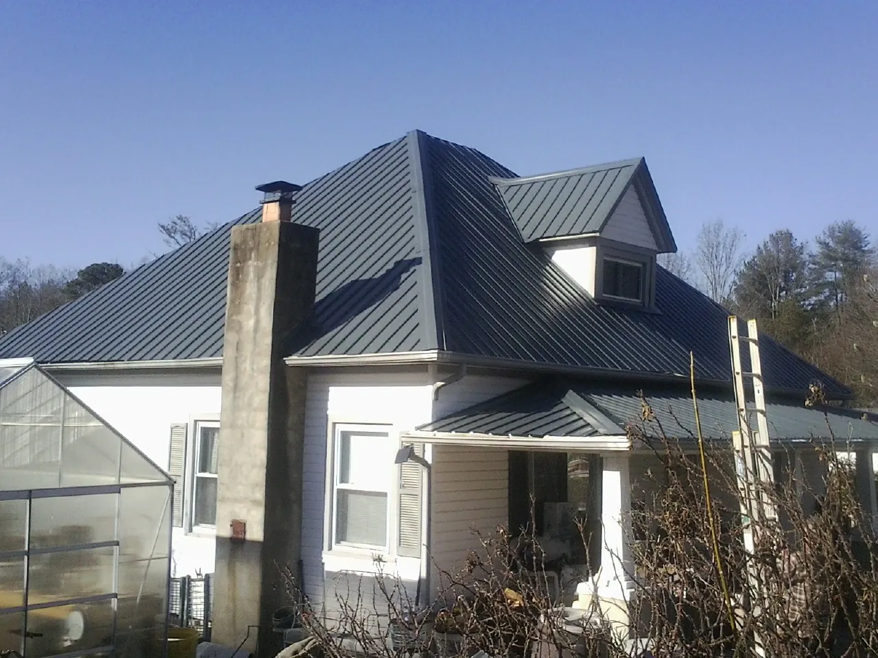 Dark blue standing seam metal roof on a white farmhouse with dormer — Slate & Tile Roof Repair by Roofing Brothers in Aleppo