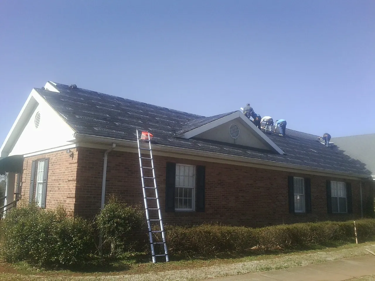 Crew tearing shingles off a brick ranch roof with a ladder set — Emergency Roof Repair work by our crew in Aleppo