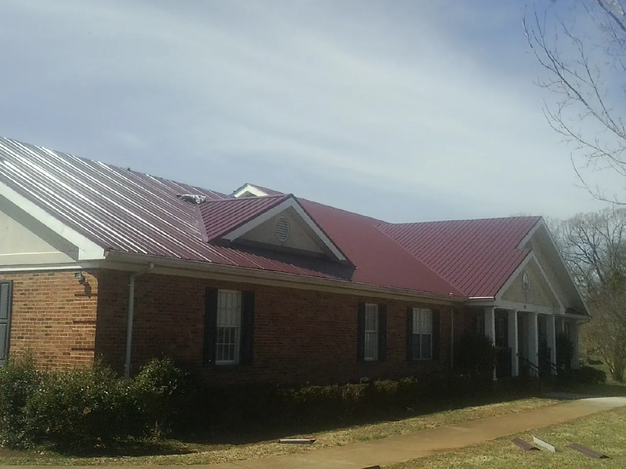 Red metal roof with gabled entries on a long brick building, from a Hail Damage Roof Repair job in Aleppo