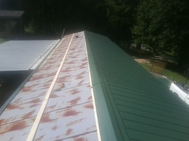 Old rusted panels beside newly installed green metal roofing — Wind Damage Roof Repair by Roofing Brothers in Aleppo