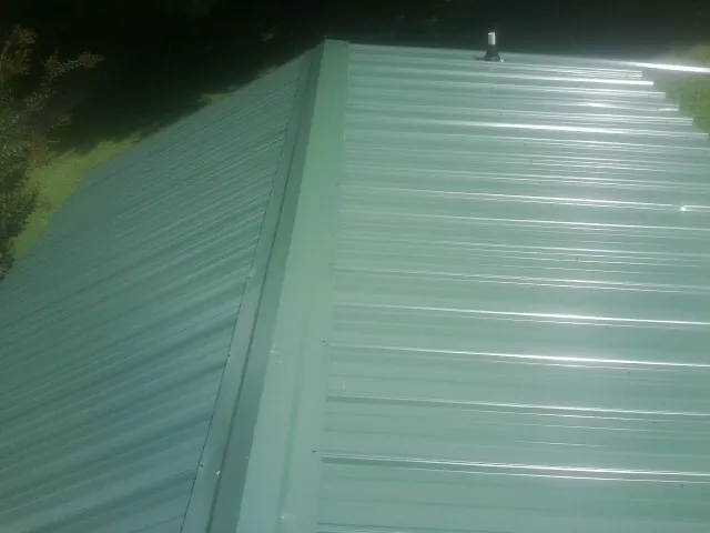 New green metal panels meeting at the ridge of a roof — Flat Roof Repair work by our crew in Aleppo