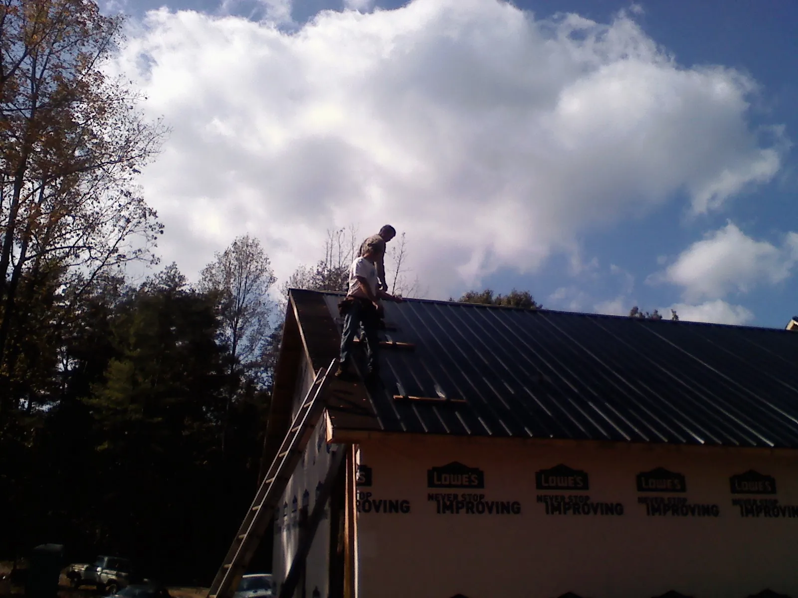 Roofer fastening dark metal panels high against a cloudy sky, from a Roof Inspection job in Aleppo
