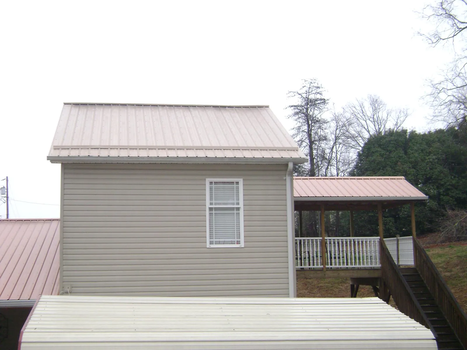 Tan metal roofs on a two story addition and attached porch, from a Roof Replacement job in Aleppo